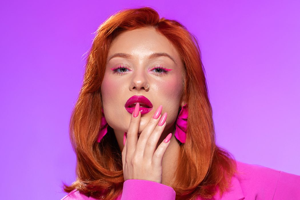 Mulher ruiva com maquilhagem e unhas rosa e blazer rosa