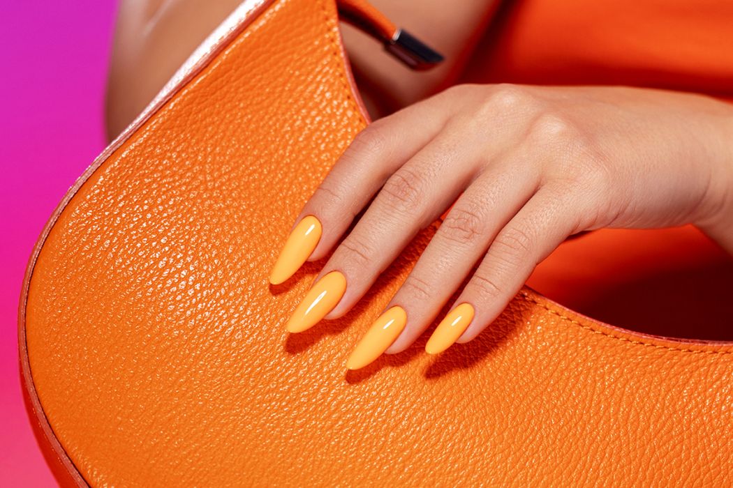 Mala de mão laranja com uma mão com unhas postiças laranja encima