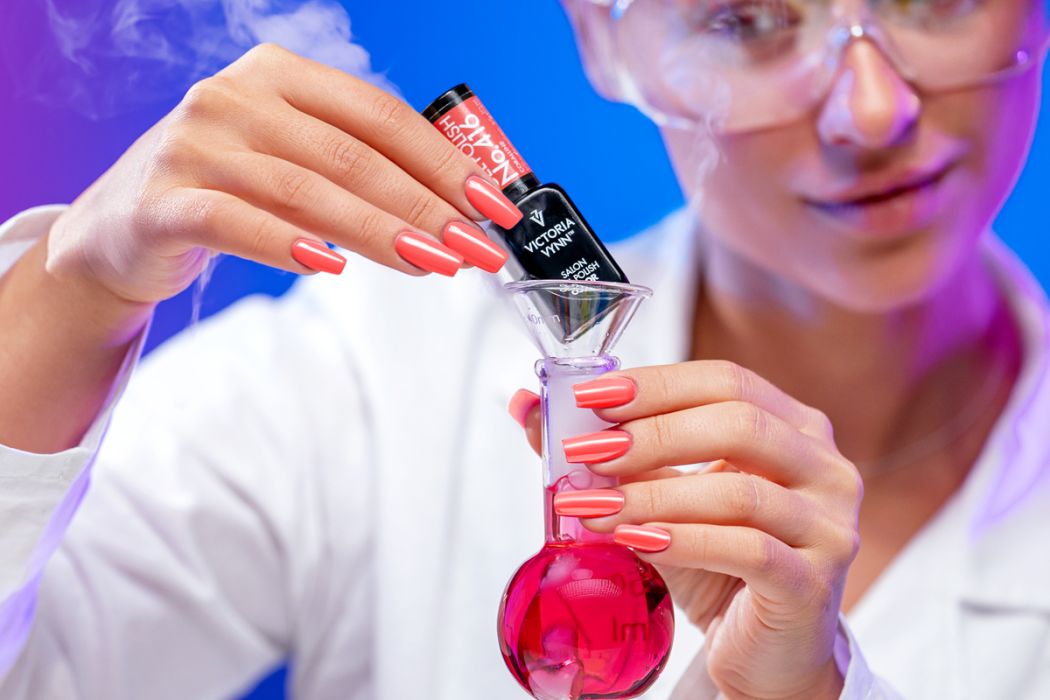 Frasco de verniz de unhas preto sendo segurado por mãos femininas com unhas coral