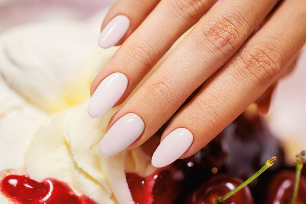 Unhas rosa pálido em formato oval com fundo de chantilly e cerejas
