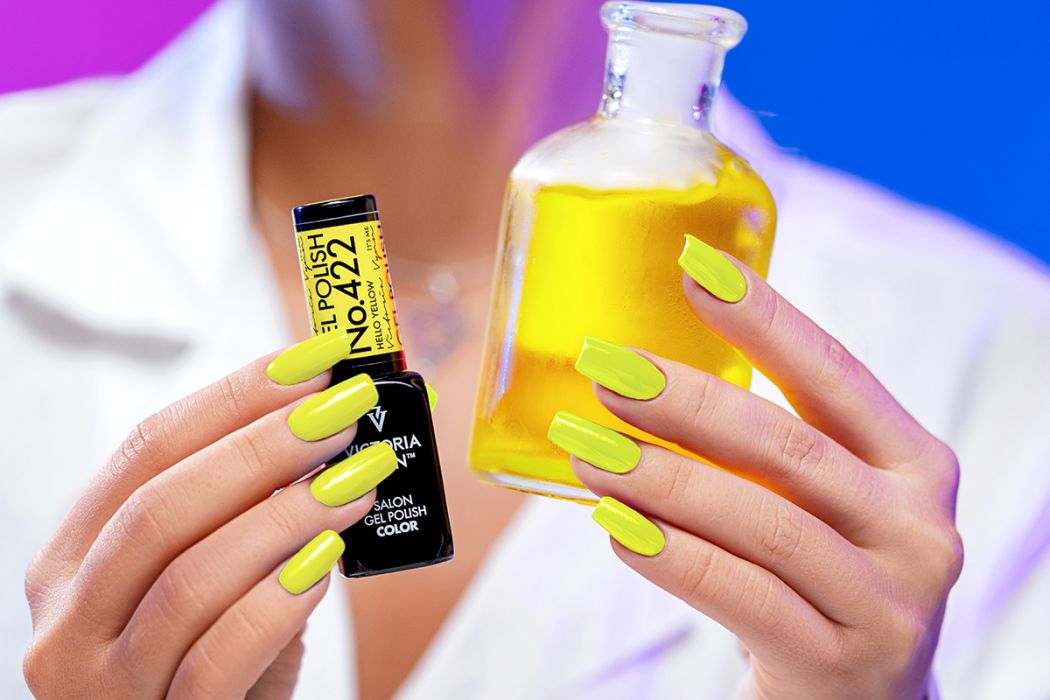Unhas pintadas com verniz amarelo segurando frasco de verniz e frasco de vidro com líquido amarelo