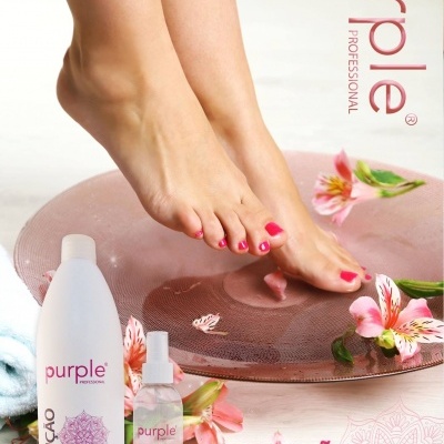 Pés femininos com verniz rosa sobre tapete rosa com flores e produtos Purple Solução Higienizante