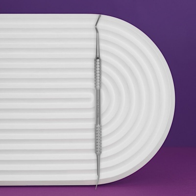 Instrumento metálico com duas pontas sobre superfície branca curva e fundo roxo