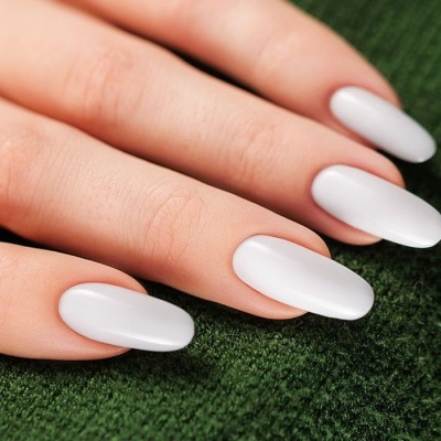 Unhas artificiais brancas em mão sobre tecido verde.