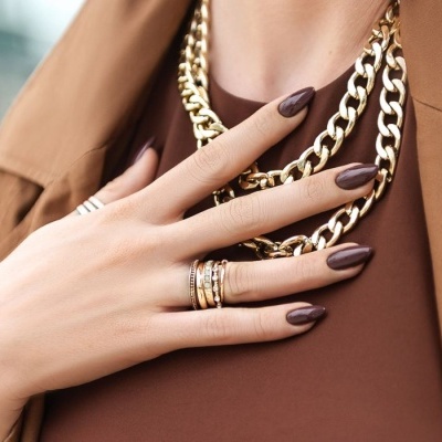 Mão feminina com anéis e colares dourados sobre roupa castanha