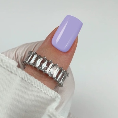 Anel prateado com pedras transparentes em dedo com unha lilás e camisola branca.