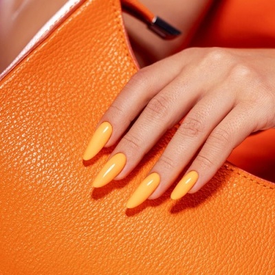 Mala de mão laranja com uma mão com unhas postiças laranja encima