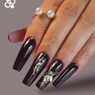 Mãos femininas com unhas negras decoradas com pedras brilhantes e anel com pérolas