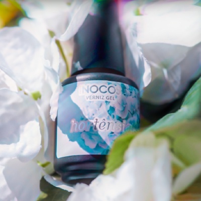 Frasco de verniz gel azul hortênsia rodeado por flores brancas