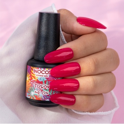 Mão feminina com unhas rosa vibrante segurando frasco de verniz INOCOS 'TURN ME ON'