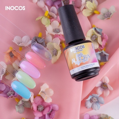 Frasco de verniz INOCOS Little Aurora com amostras de unhas coloridas e flores artificiais numa superfície rosa