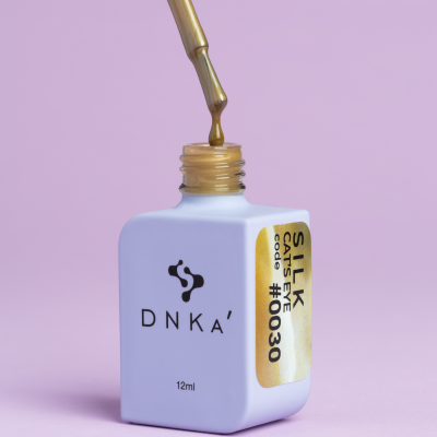 Frasco branco de esmalte DNKA com rótulo dourado e tampa dourada, fundo rosa