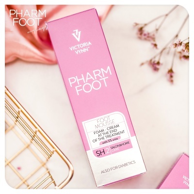 Embalagem rosa e branca do produto PHARM FOOT Victoria Vynn sobre superfície branca com flores secas ao lado.