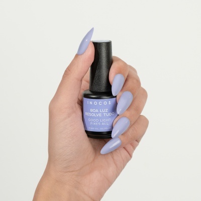 Frasco de verniz gel lilás da marca INOCOS nas mãos de mulher, com unhas pintadas da mesma cor.