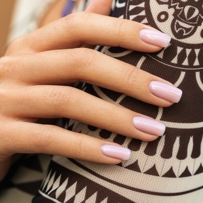 Mão feminina com unhas rosa claro sobre tecido preto e branco com padrão geométrico