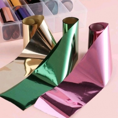 Folhas e rolos de papel metalizado em várias cores sobre superfície rosa
