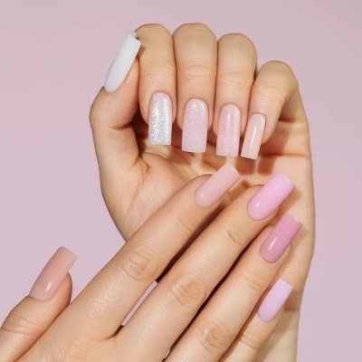Mãos femininas com unhas postiças longas em tons variados de rosa e branco.