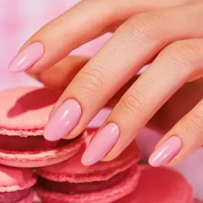 Mão com unhas rosa a tocar em macarons cor de rosa.
