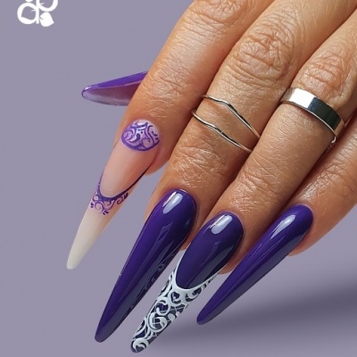 Unhas compridas decoradas com verniz roxo e desenhos brancos e roxos, anéis prateados, fundo roxo