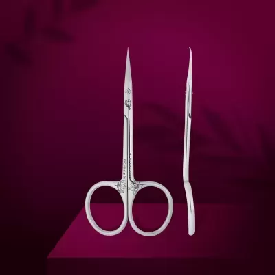 Tesouras de manicure em metal prateado com detalhes gravados sobre fundo roxo