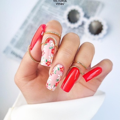 Unhas em gel vermelhas e florais com anéis dourados e fundo desfocado