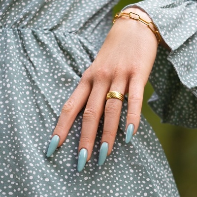 Mão feminina com unhas azul claro e jóias douradas sobre vestido verde com bolinhas brancas