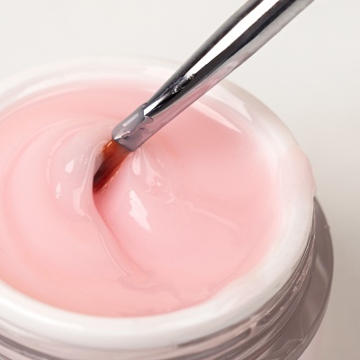 Frasco aberto de creme rosa com pincel metalizado dentro do frasco.