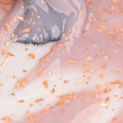 Pincel com cerdas pretas aplicado em superfície cor-de-rosa brilhante com partículas douradas.