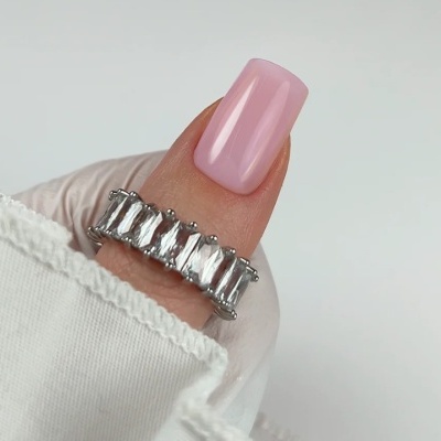 anel prateado com pedras transparentes retangulares num dedo de unha rosa claro