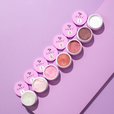 Potes de cremes coloridos com tampas cor-de-rosa DNKA sobre superfície roxa