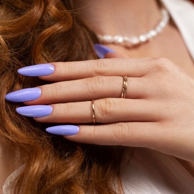 Mão feminina com unhas lilás compridas e anéis dourados