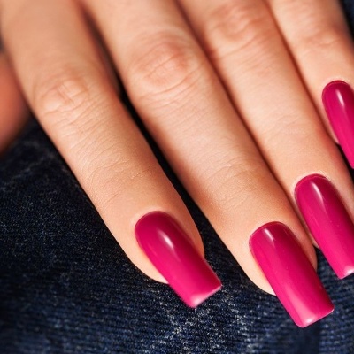 Unhas longas pintadas de rosa vibrante sobre tecido de ganga