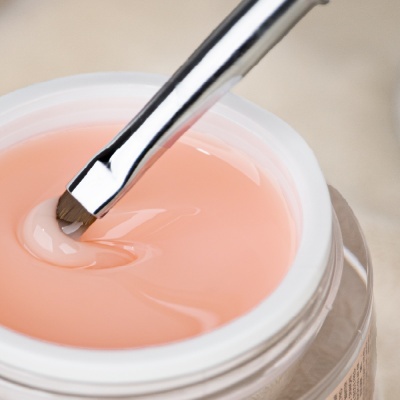 Pote de creme cor de pêssego com pincel metálico num fundo neutro