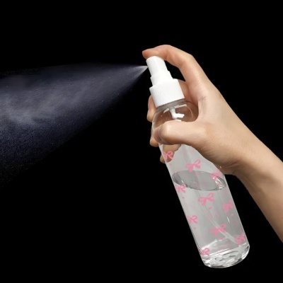 Frasco spray transparente com tampa branca e desenhos cor-de-rosa, spray a ser disparado.
