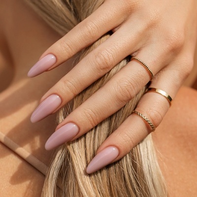 Mão feminina com unhas rosas e anéis dourados segurando cabelo loiro