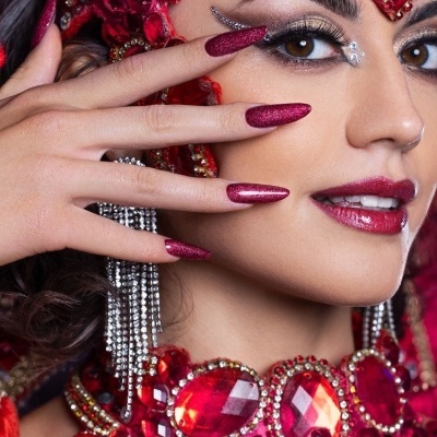 Mão feminina com unhas longas vinho brilhante e acessórios vermelhos com pedras grandes