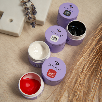 Frascos de tinta gel para unhas DNKA em vermelho, branco e preto sobre tecido bege com elementos decorativos.