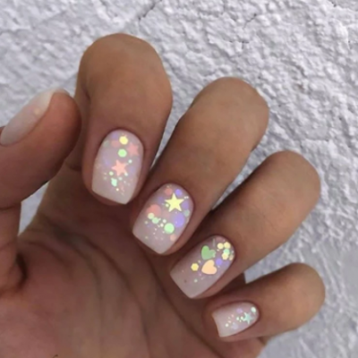 Unhas com verniz nude claro e decoração holográfica de corações e estrelas