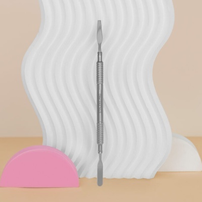 Espátula dupla de metal prateado com fundo decorativo branco ondulado e meia-lua rosa