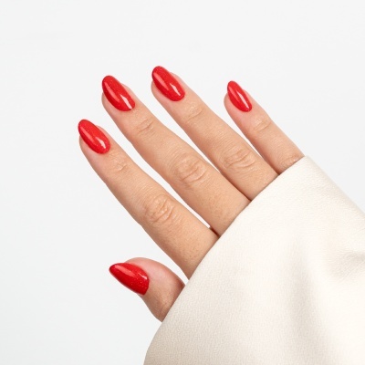 Mão feminina com unhas vermelhas brilhantes e manga branca.