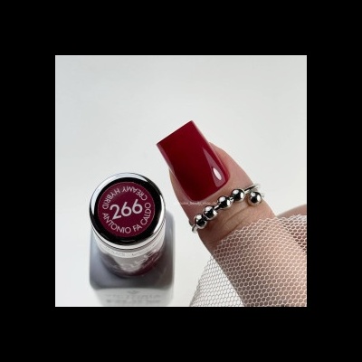 Frasco de verniz vermelho escuro com texto, mão com unha pintada e anel prateado