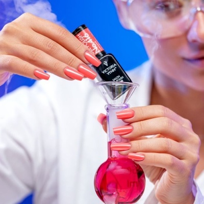 Frasco de verniz de unhas preto sendo segurado por mãos femininas com unhas coral