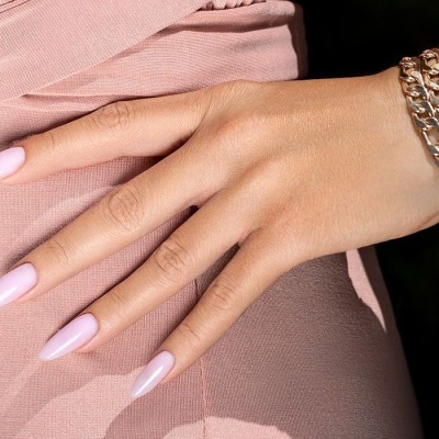 Mão feminina com unhas rosa claro e pulseira dourada sobre tecido rosa
