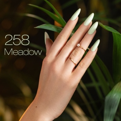 Mão feminina com unhas pintadas de verde claro com folhas verdes ao fundo