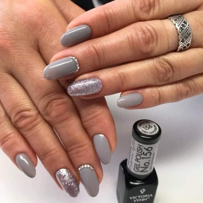 Unhas pintadas com verniz gel cinzento e glitter com cristais e garrafa de verniz gel