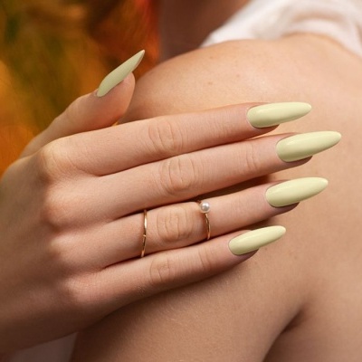 Mão com unhas verdes longas e anéis dourados com pérola sobre ombro