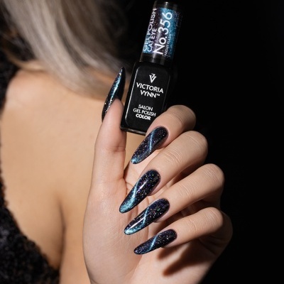 Mão feminina com unhas longas pintadas com verniz gel cat eye preto azulado segurando frasco de verniz VICTORIA VYNN