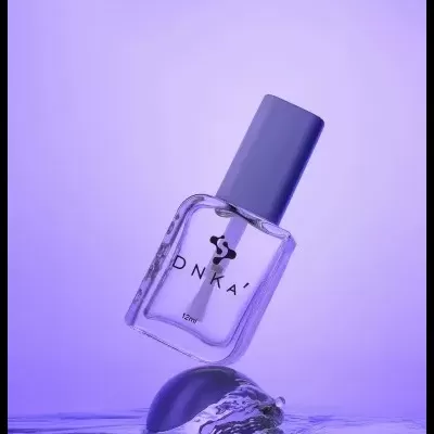 Frasco de verniz para unhas DNKA com tampa azul sobre superfície de água lilás