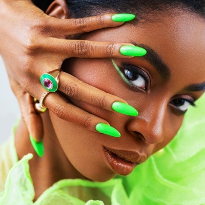 Close-up de mulher com unhas verdes, maquiagem verde e anéis dourados