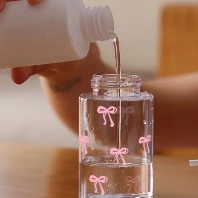 Frasco transparente com laços cor-de-rosa sendo enchido com líquido